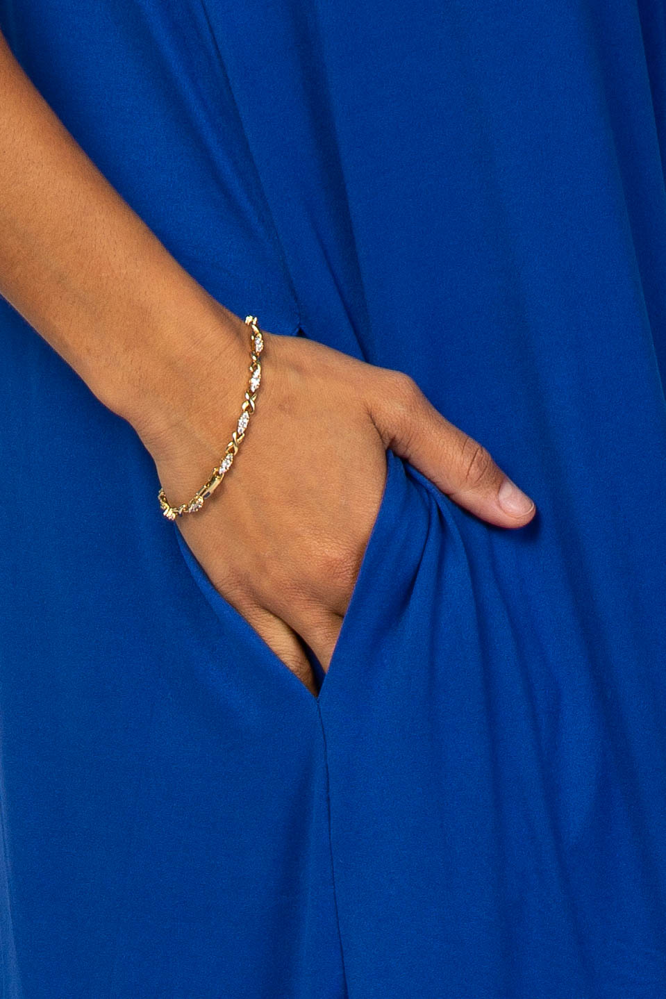 woman wearing a bright blue dress with side pockets and a gold bracelet on her wrist