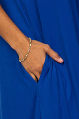 woman wearing a bright blue dress with side pockets and a gold bracelet on her wrist