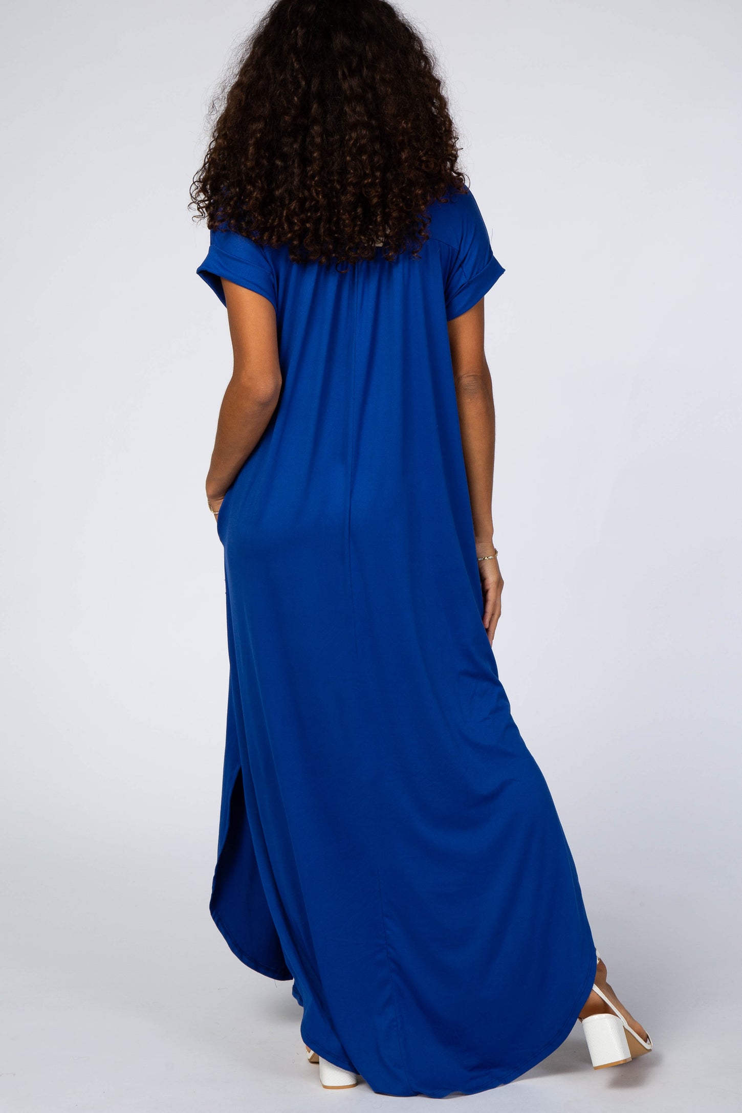 woman wearing a long blue maxi dress with short sleeves and side pockets, viewed from the back