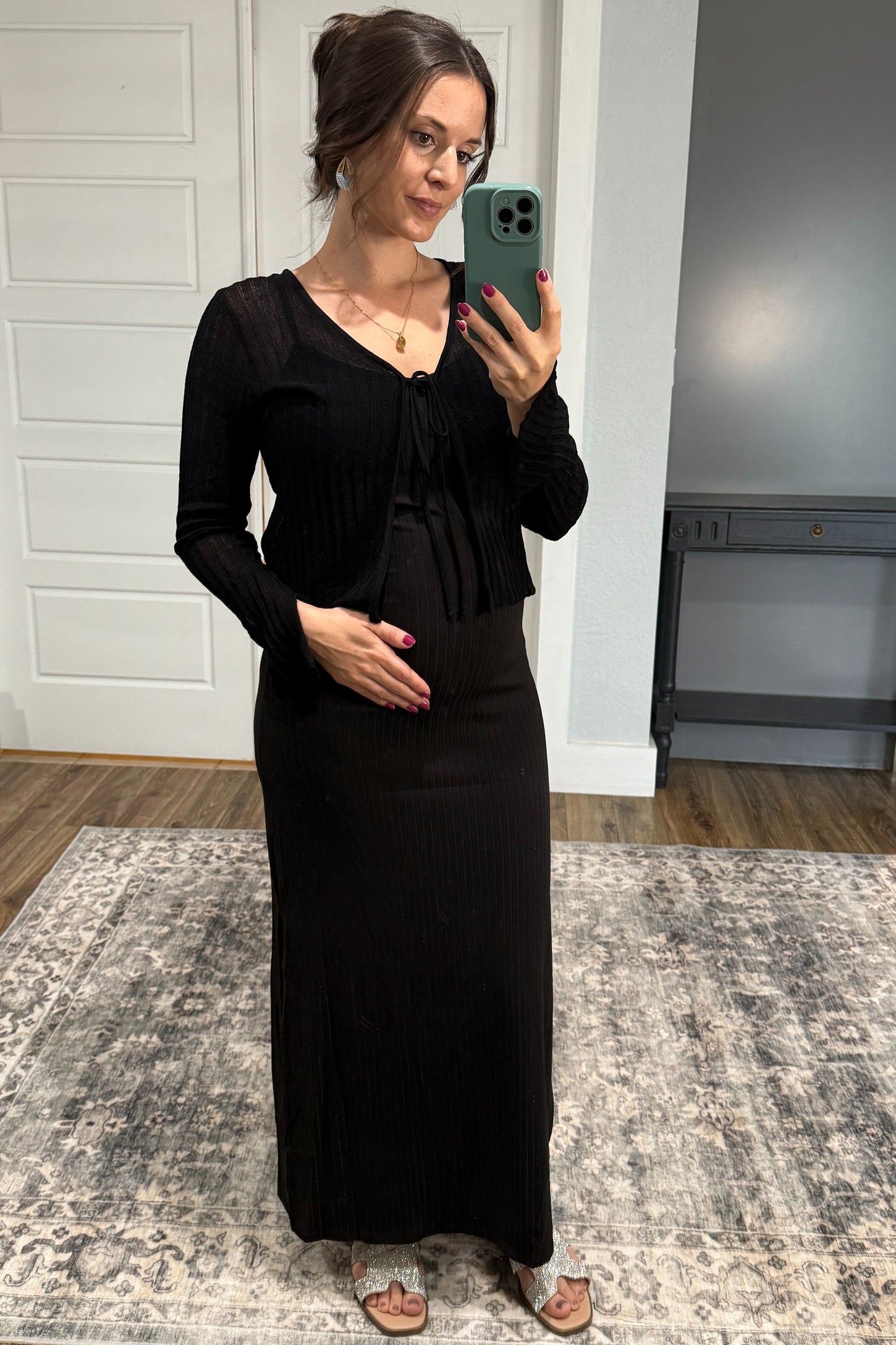 woman wearing a black ribbed maternity dress with a tie-front cardigan, showing her baby bump while posing in a mirror