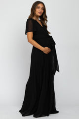 woman wearing a black chiffon maternity maxi dress with short flutter sleeves and a tied waist, showing her baby bump