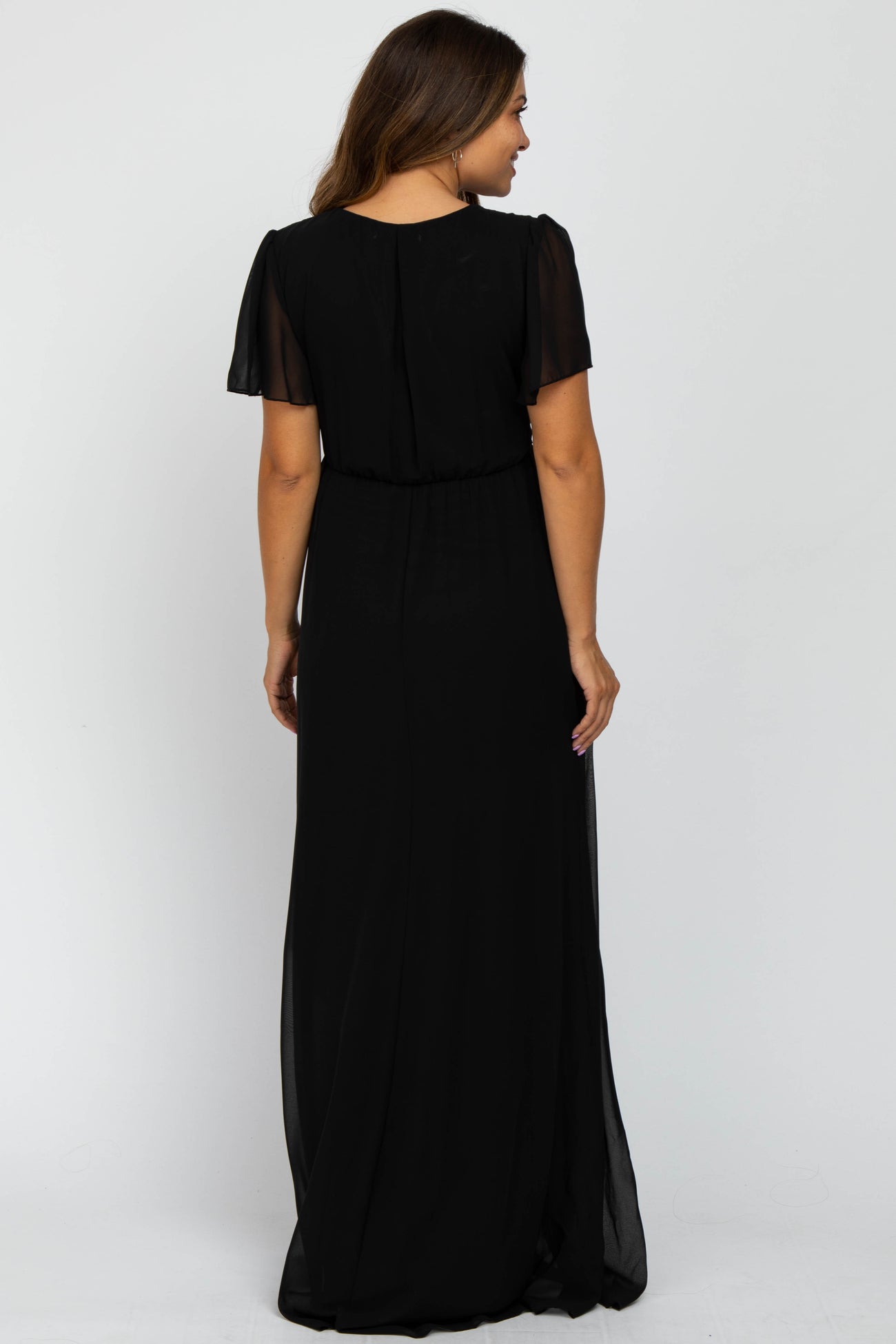 woman wearing a black maternity maxi dress with short sheer sleeves and a gathered waist, shown from the back