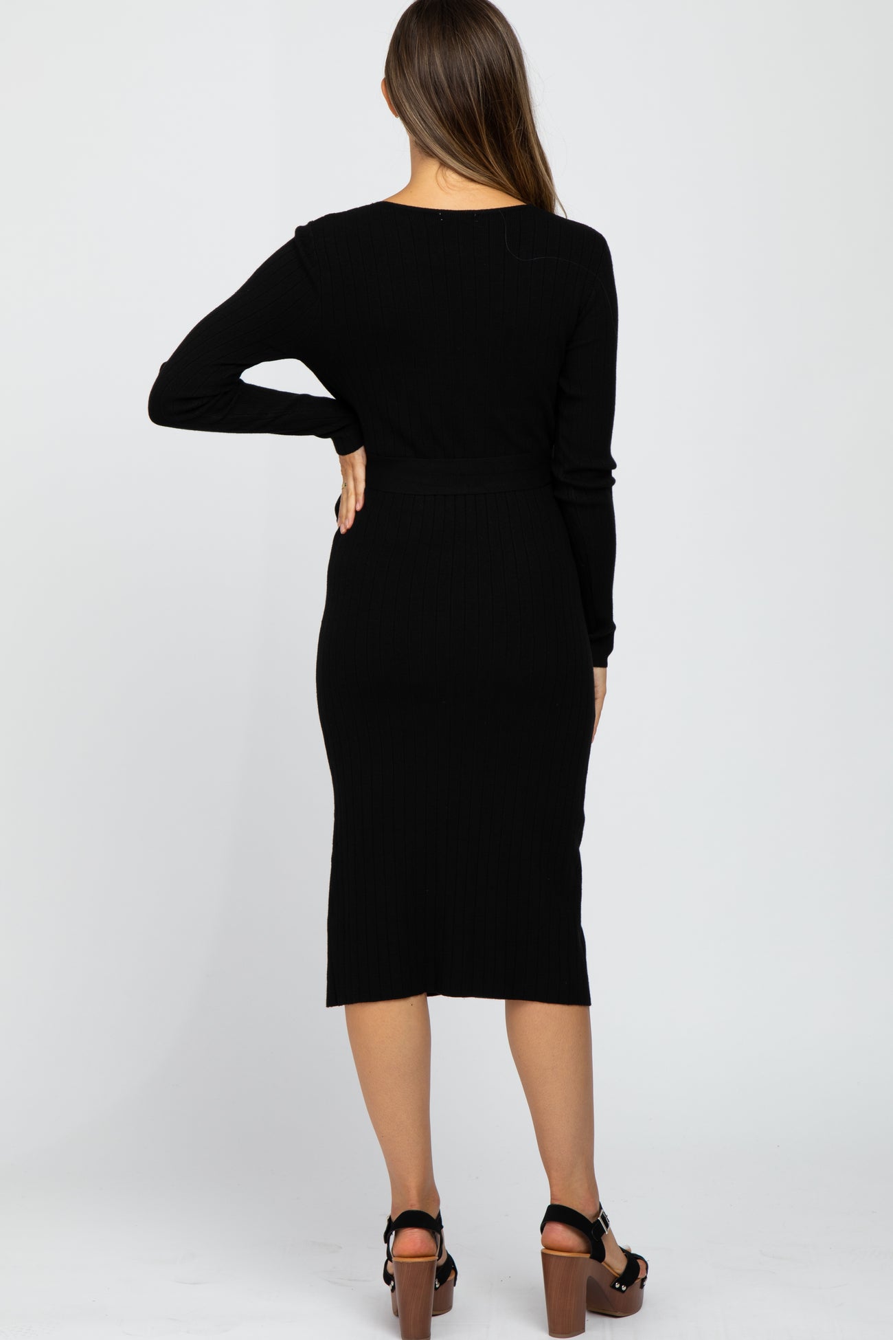 Back view of a woman wearing a black long sleeve ribbed midi dress with a belted waist and platform sandals
