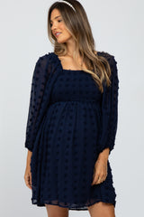 woman wearing a navy blue maternity dress with puff sleeves and textured dots, showing her baby bump