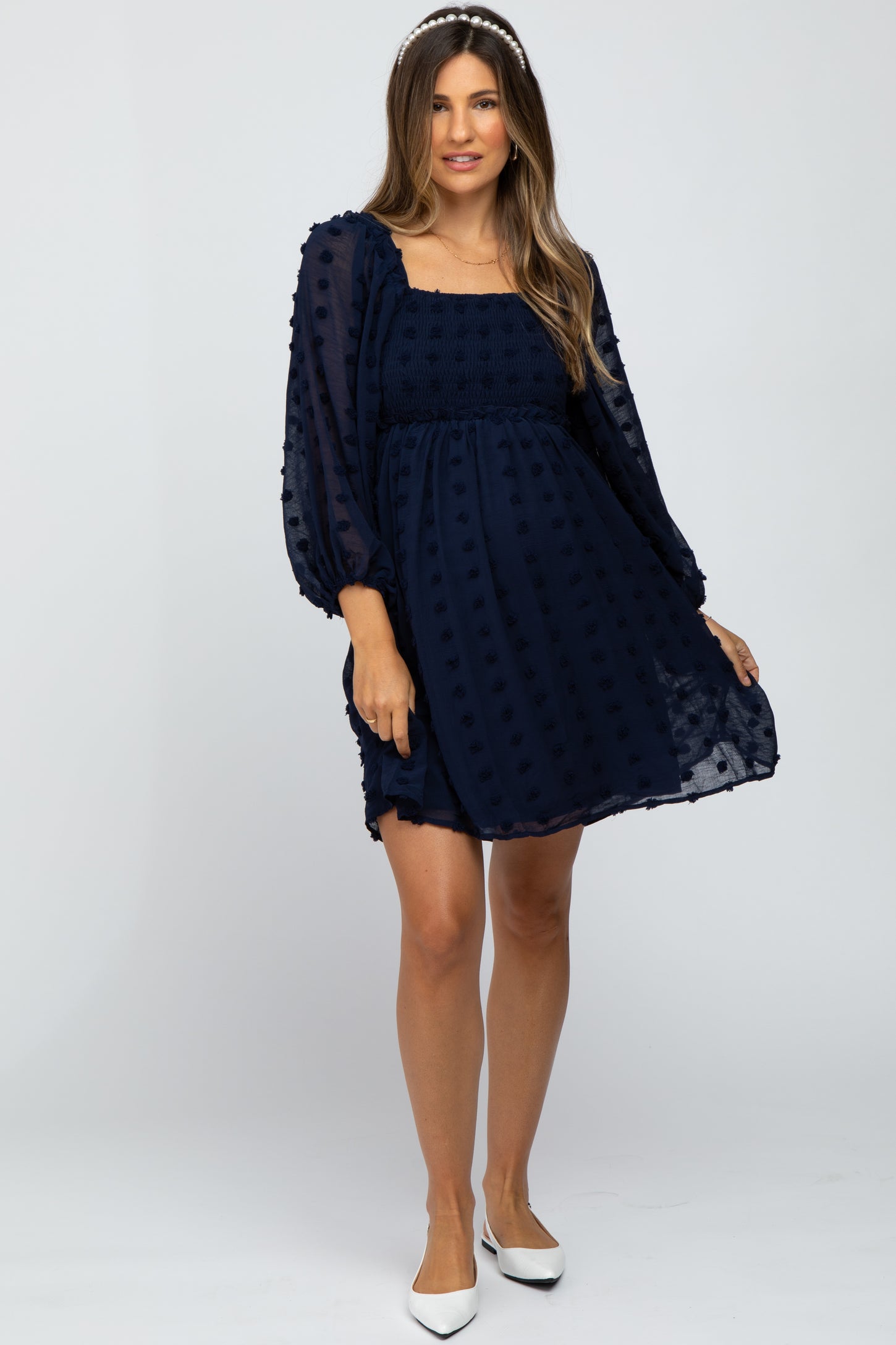 woman wearing a navy blue maternity dress with puff sleeves and textured dot details, showing her baby bump