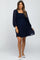 woman wearing a navy blue maternity dress with puff sleeves and textured dot details, showing her baby bump