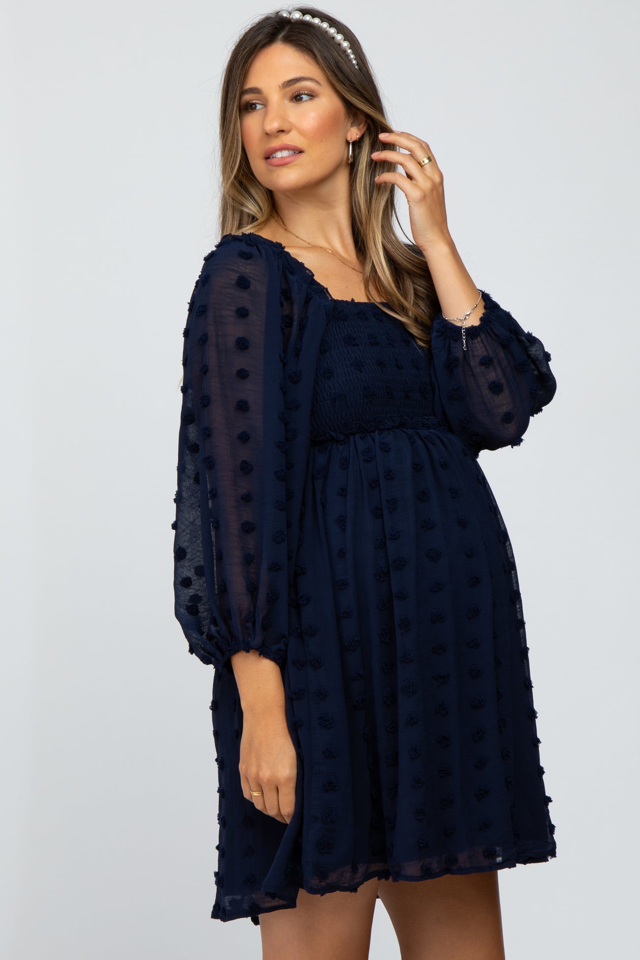 woman wearing a navy blue maternity dress with puff sleeves and textured dots, showcasing her baby bump