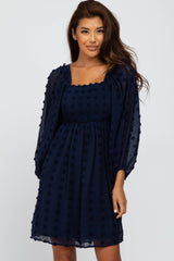 woman wearing a navy blue dress with puff sleeves and textured dot detailing on the fabric