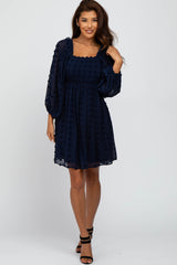 woman wearing a navy blue short puff sleeve dress with a textured bodice and a flowy skirt, standing in a relaxed pose