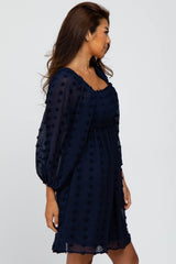 woman wearing a navy blue swiss dot maternity dress with long puff sleeves and smocked bodice