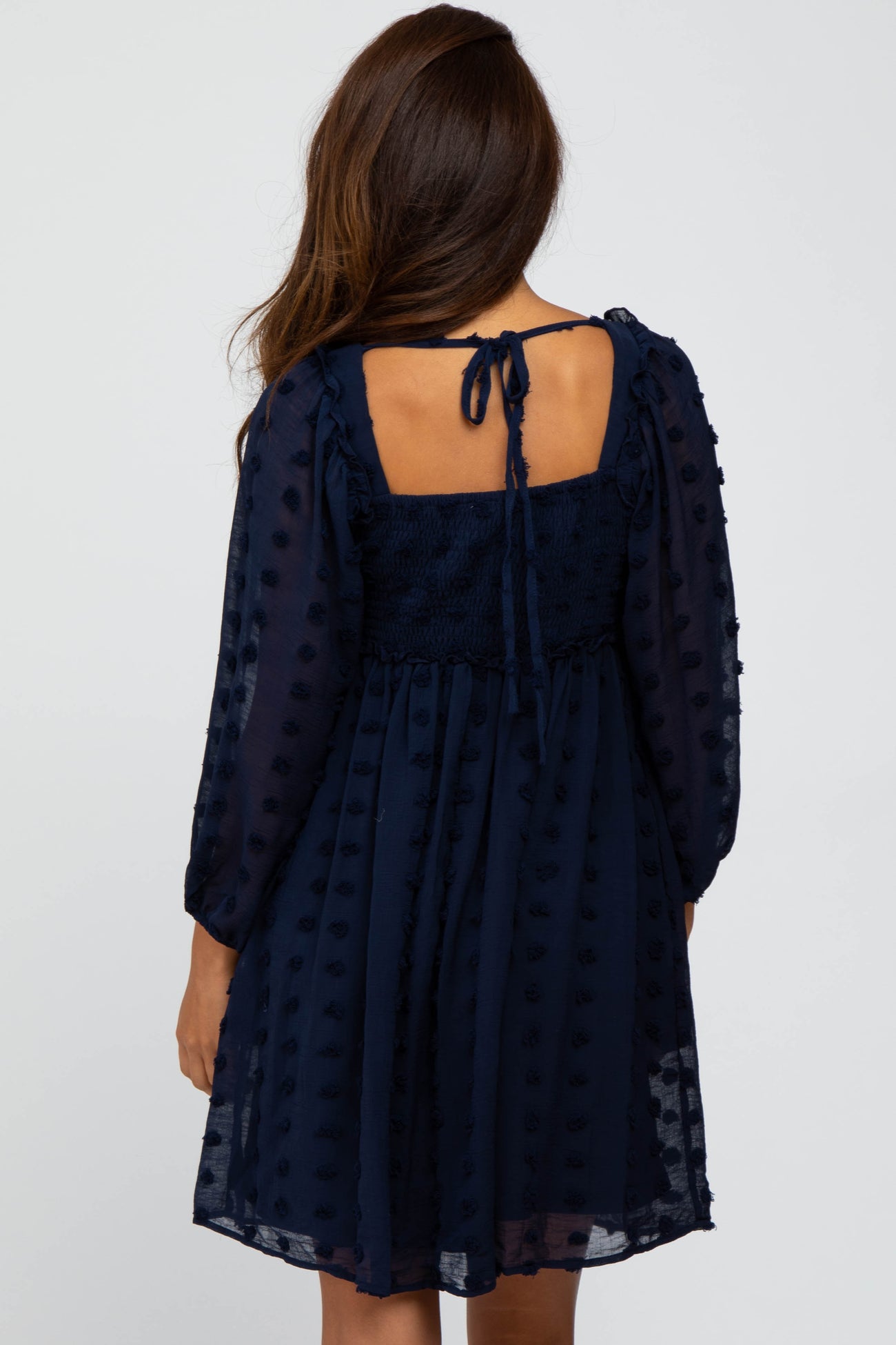 women wearing a navy blue short dress with puff sleeves and a back tie detail, featuring textured dots throughout