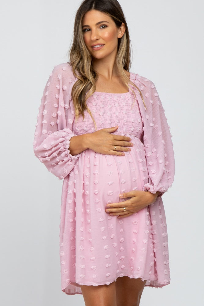 woman wearing a pink smocked maternity dress with puff sleeves and holding her baby bump