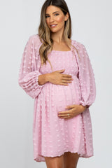 woman wearing a pink smocked maternity dress with puff sleeves and holding her baby bump