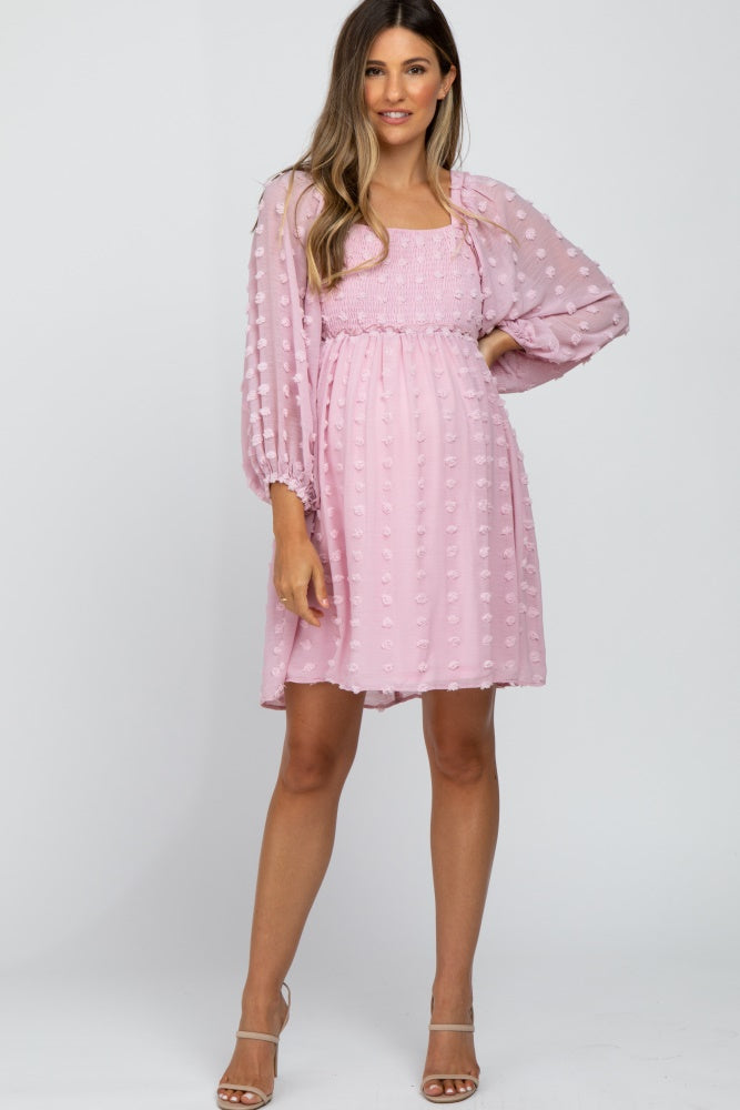 woman wearing a pink maternity dress with textured dots and sheer balloon sleeves, showcasing her baby bump