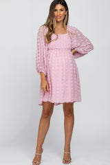 woman wearing a pink maternity dress with textured dots and sheer balloon sleeves, showcasing her baby bump