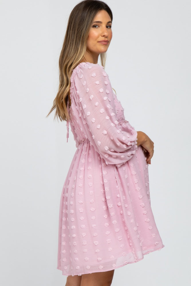 woman wearing a pink maternity dress with textured dots and puff sleeves, showing her baby bump
