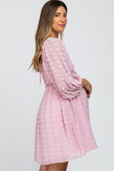 woman wearing a pink maternity dress with textured dots and puff sleeves, showing her baby bump