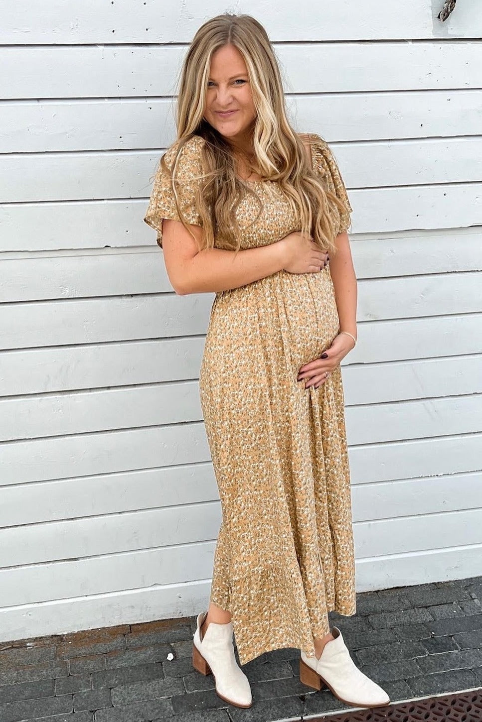 woman wearing a mustard floral maternity dress and holding her baby bump