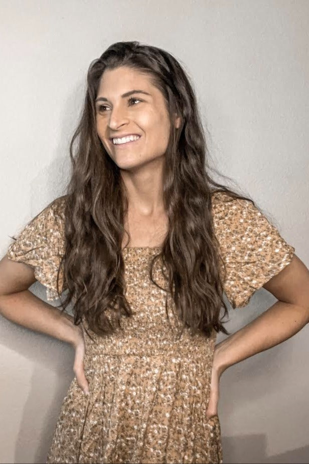 woman wearing a floral print smocked dress with short sleeves and a square neckline, smiling and posing with hands on hips