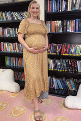 woman wearing a mustard yellow maternity dress with a floral pattern and holding her baby bump in a bookstore