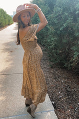 woman wearing a brown floral off-shoulder maternity dress and showing her baby bump while posing outdoors