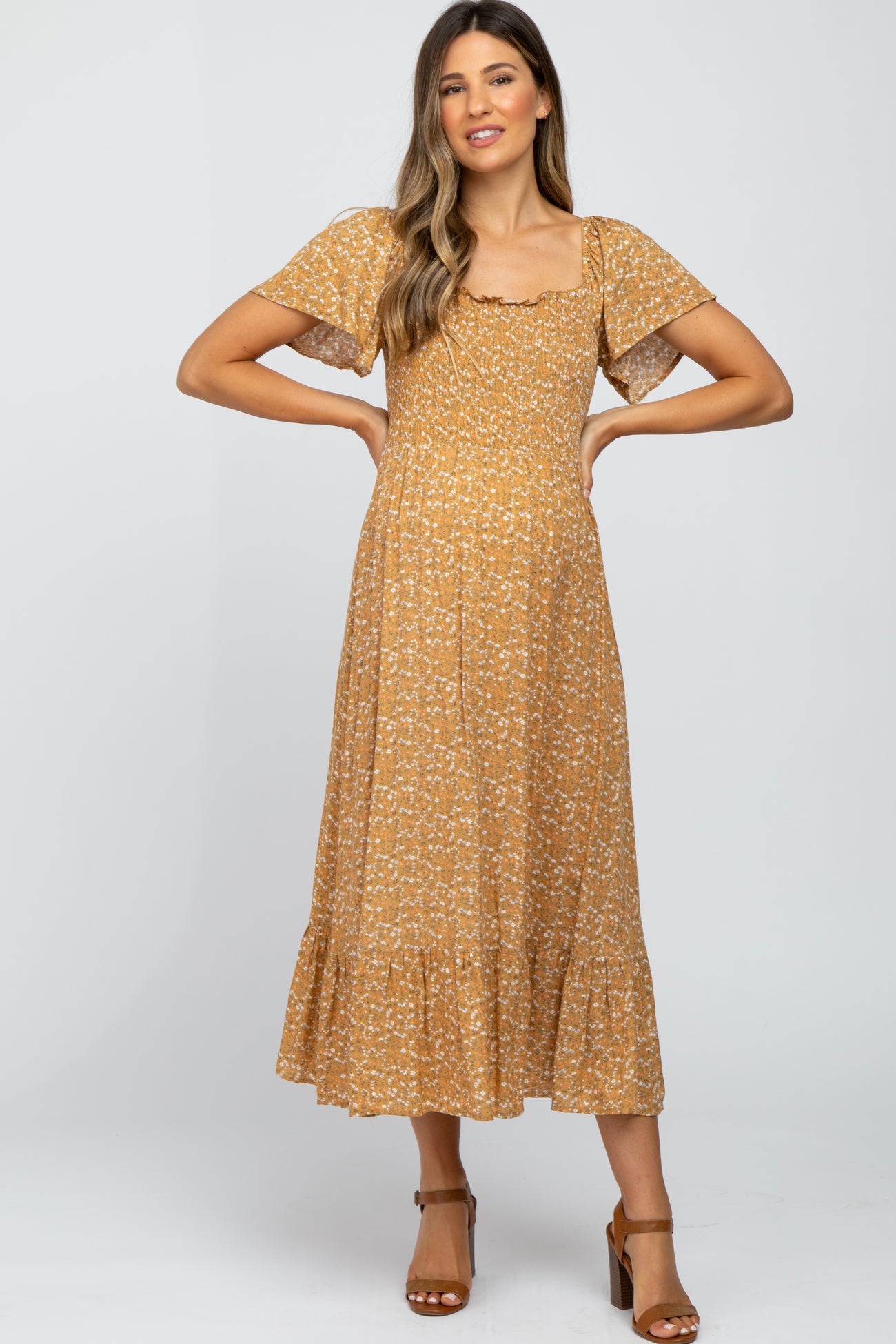 woman wearing a mustard floral print maternity dress with flutter sleeves and a ruffled hem, showing her baby bump