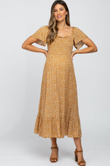 woman wearing a mustard floral print maternity dress with flutter sleeves and a ruffled hem, showing her baby bump