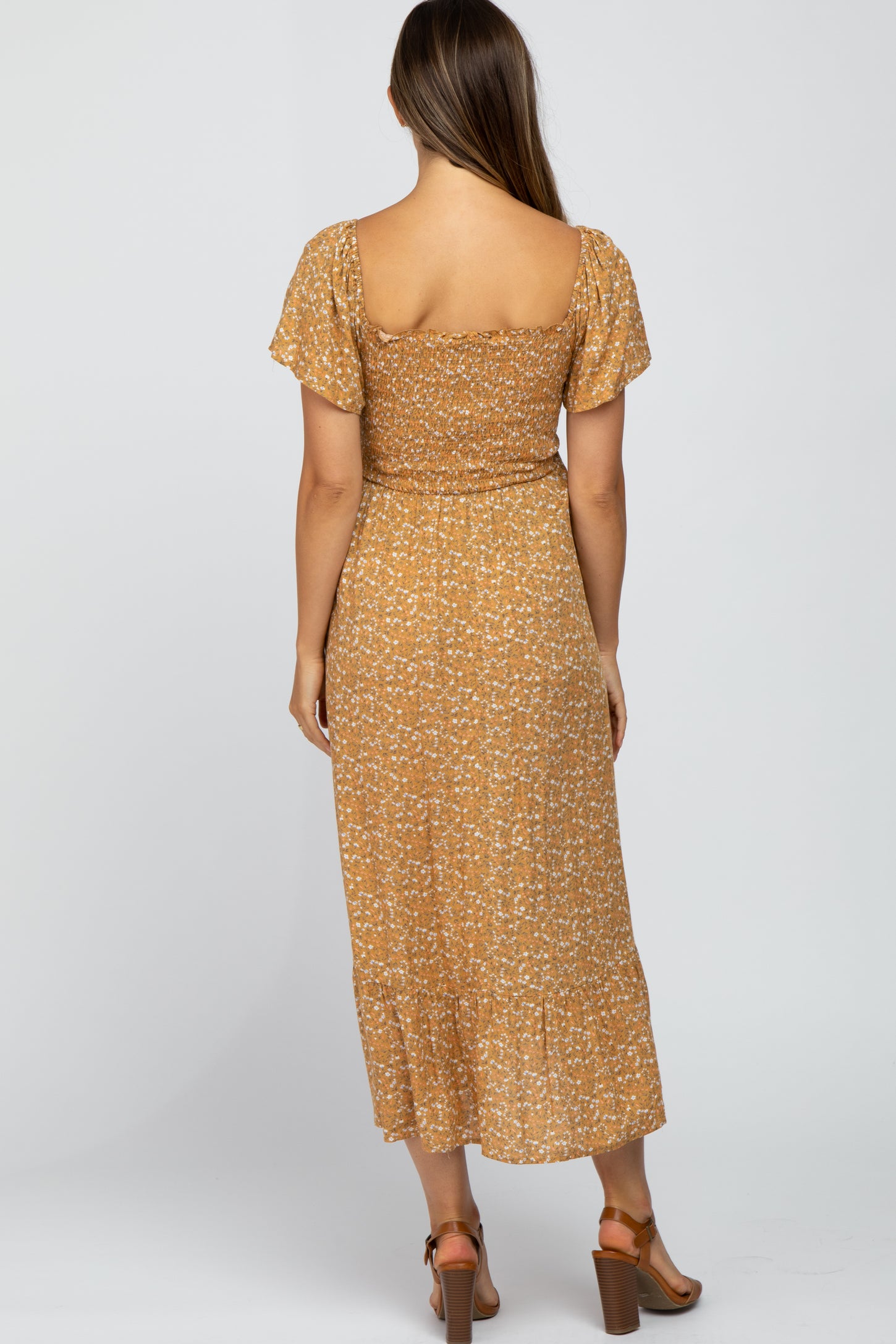 woman wearing a mustard yellow floral maternity dress with short sleeves and a flowy hem, showing her baby bump from the back