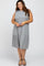 smiling woman wearing a sleeveless grey tiered midi dress and black strappy sandals
