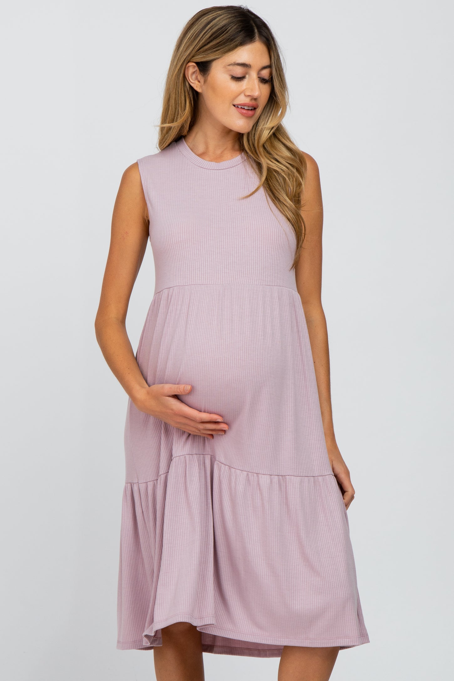 Pregnant woman wearing a mauve sleeveless ribbed maternity dress with a tiered skirt