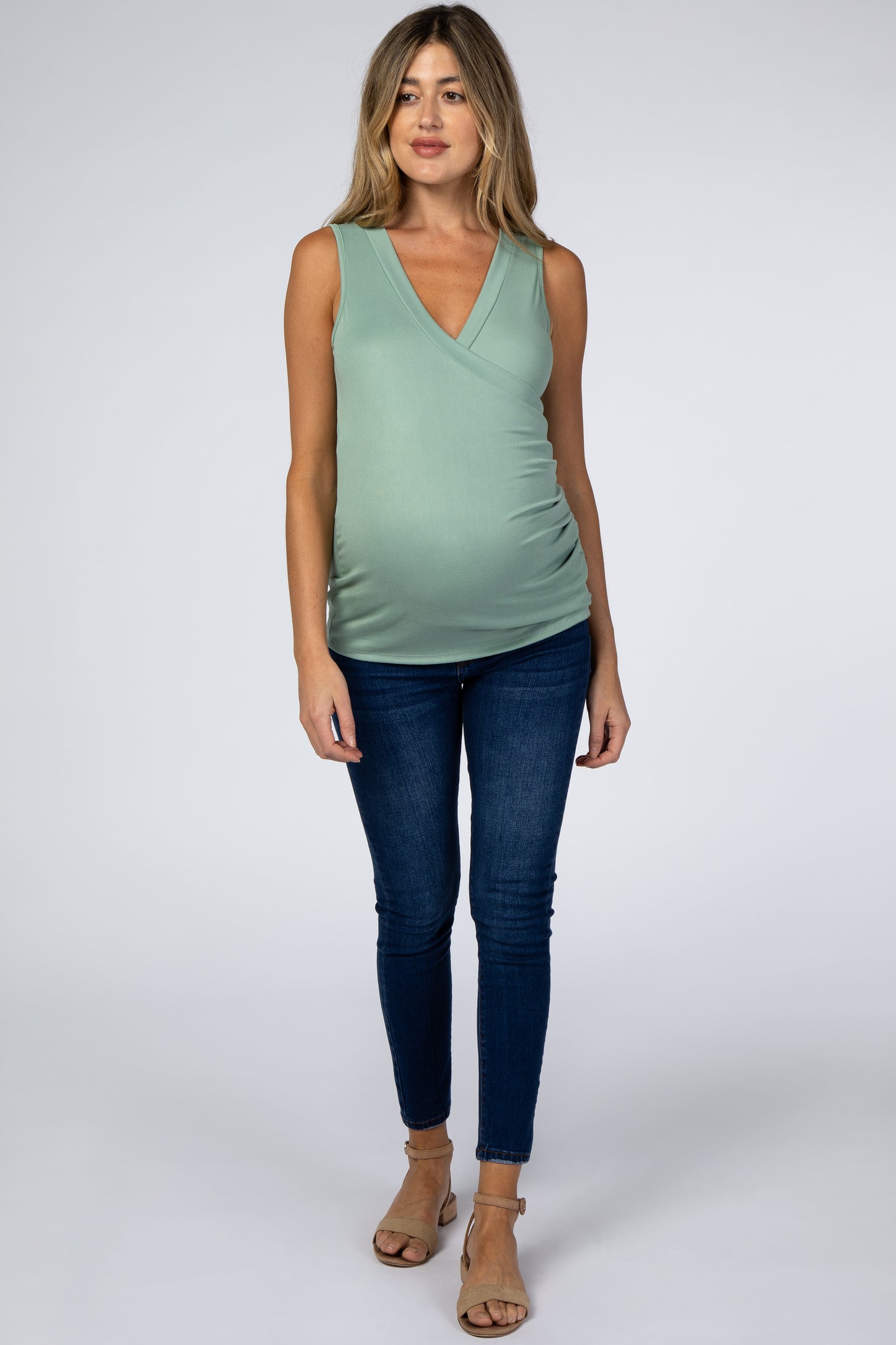 woman wearing a mint green maternity top with a v-neck and baby bump, paired with blue skinny jeans