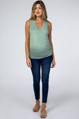 woman wearing a mint green maternity top with a v-neck and baby bump, paired with blue skinny jeans