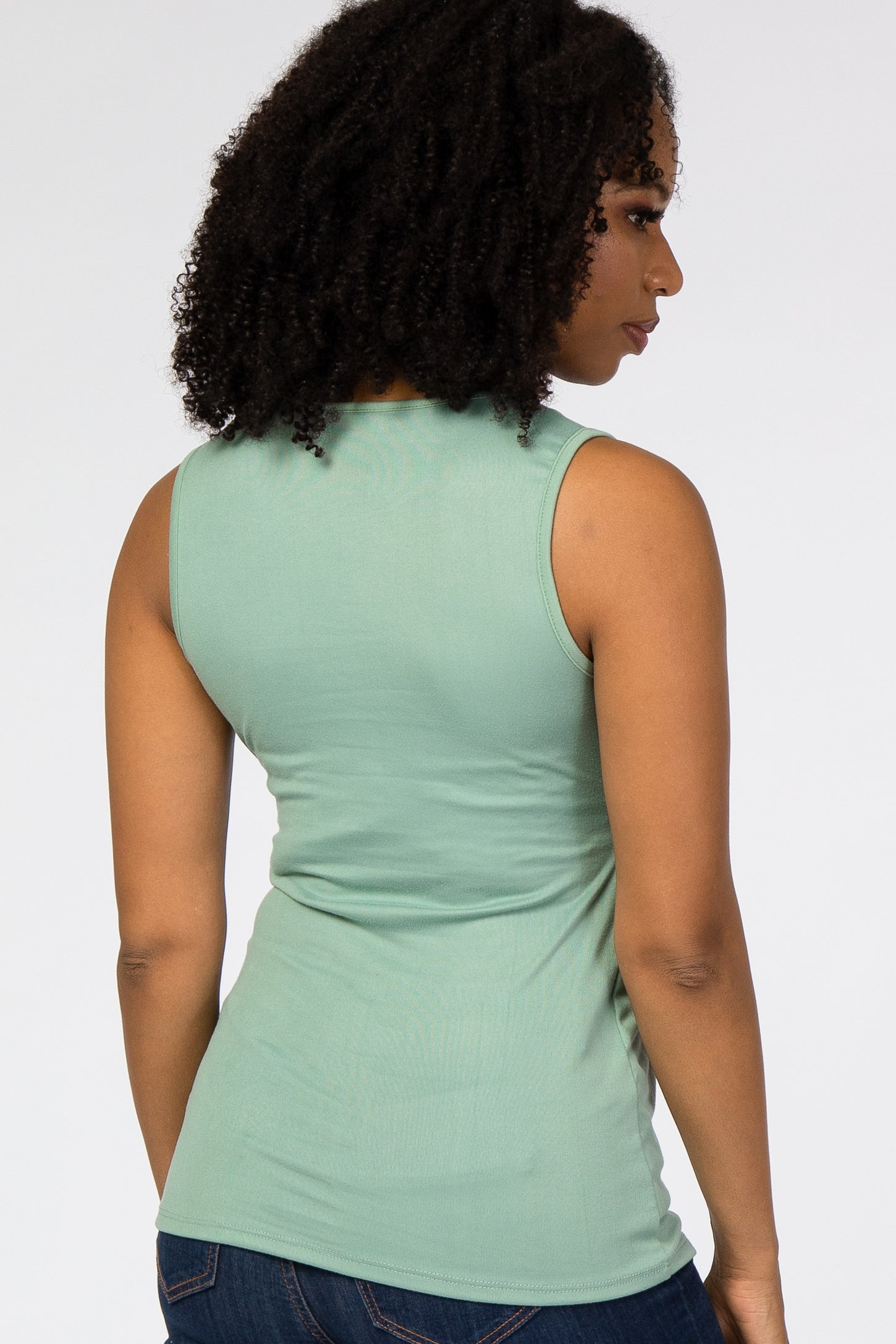woman wearing a mint green sleeveless top, seen from the back, paired with dark blue jeans