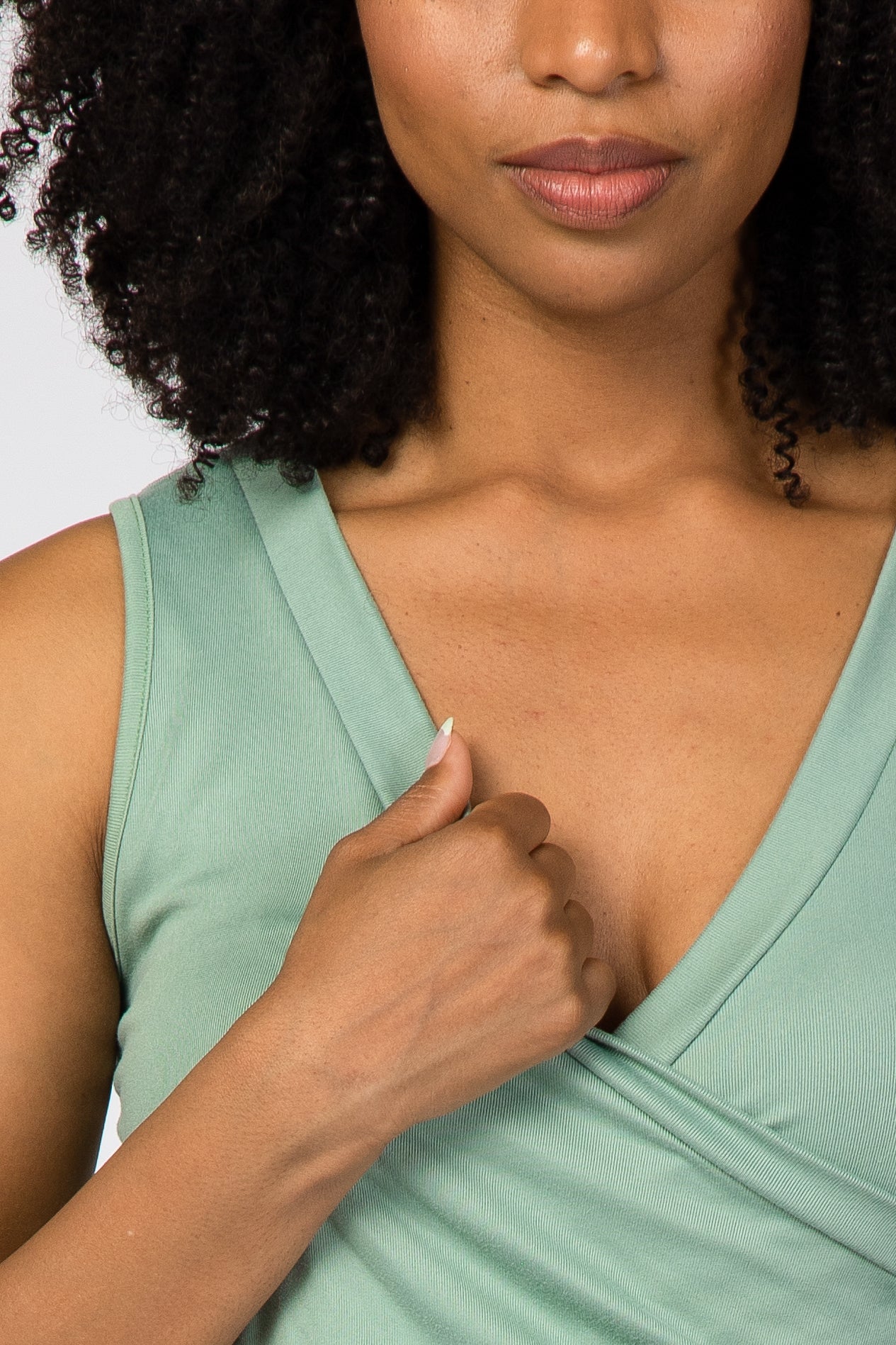 woman wearing a green sleeveless wrap top, holding the fabric at the neckline