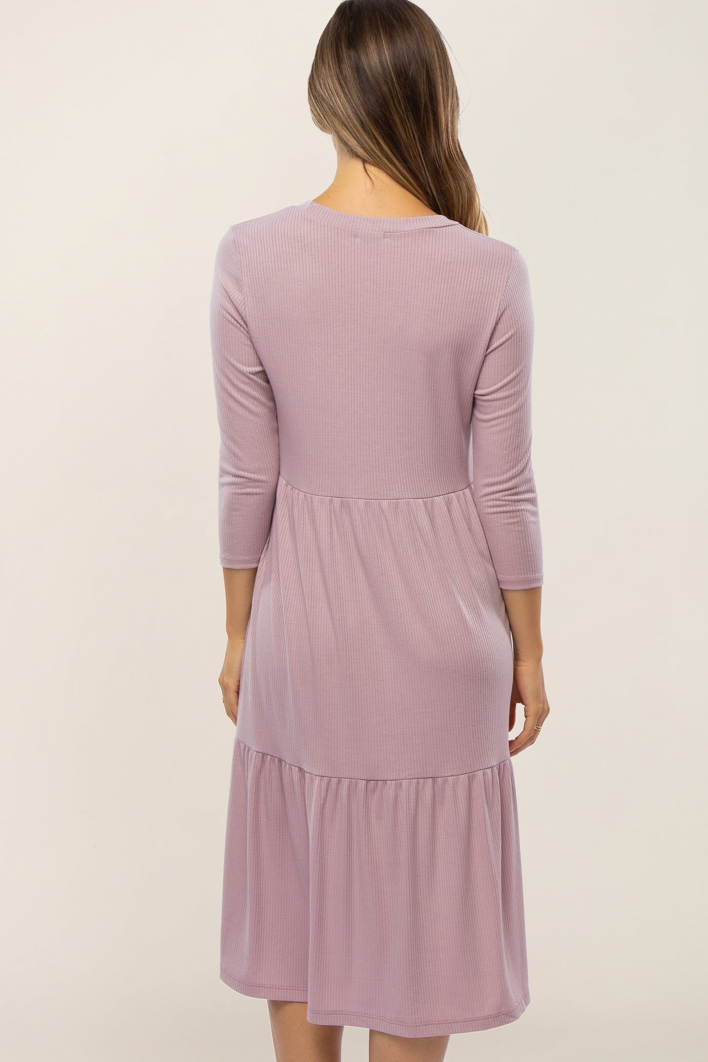 Back view of a woman wearing a mauve ribbed knit tiered midi dress with three-quarter sleeves