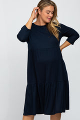 Pregnant woman wearing a navy blue ribbed maternity dress with three-quarter sleeves and tiered skirt