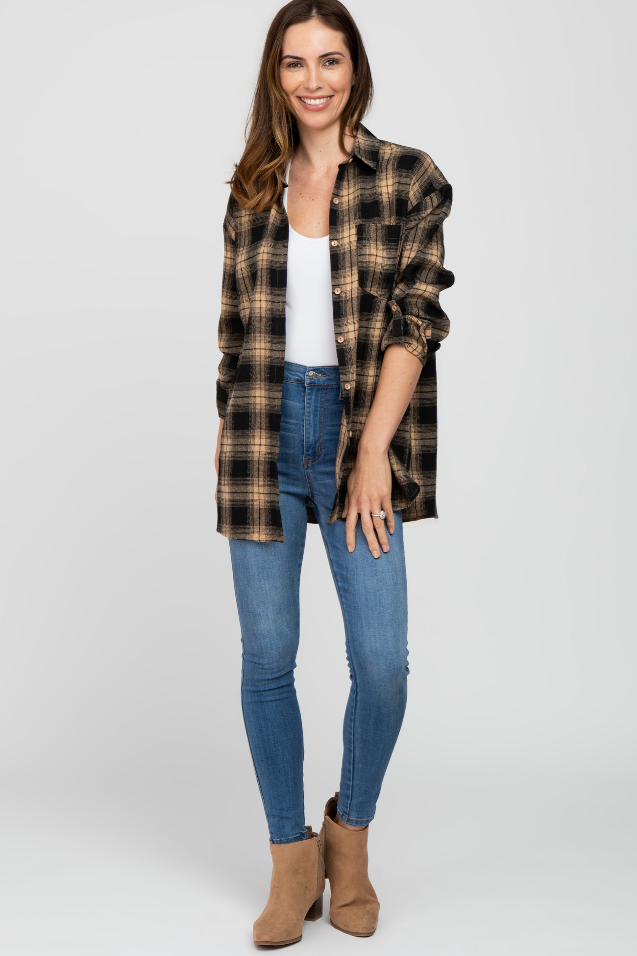 woman wearing a black and tan plaid oversized shirt, white tank top, and blue skinny jeans with tan ankle boots