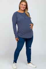Smiling pregnant woman wearing a blue long sleeve maternity top and distressed jeans with white sneakers