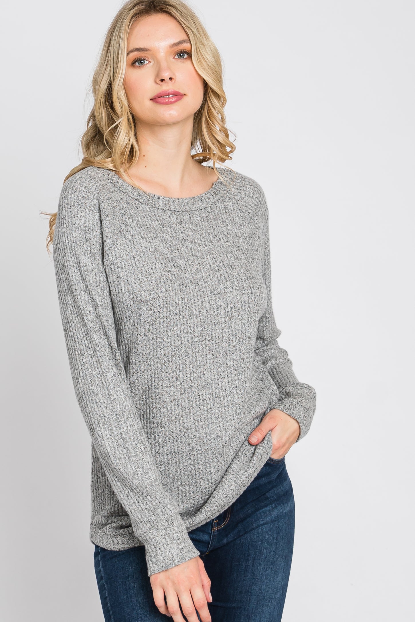 blonde woman wearing a grey long sleeve waffle knit sweater and blue jeans