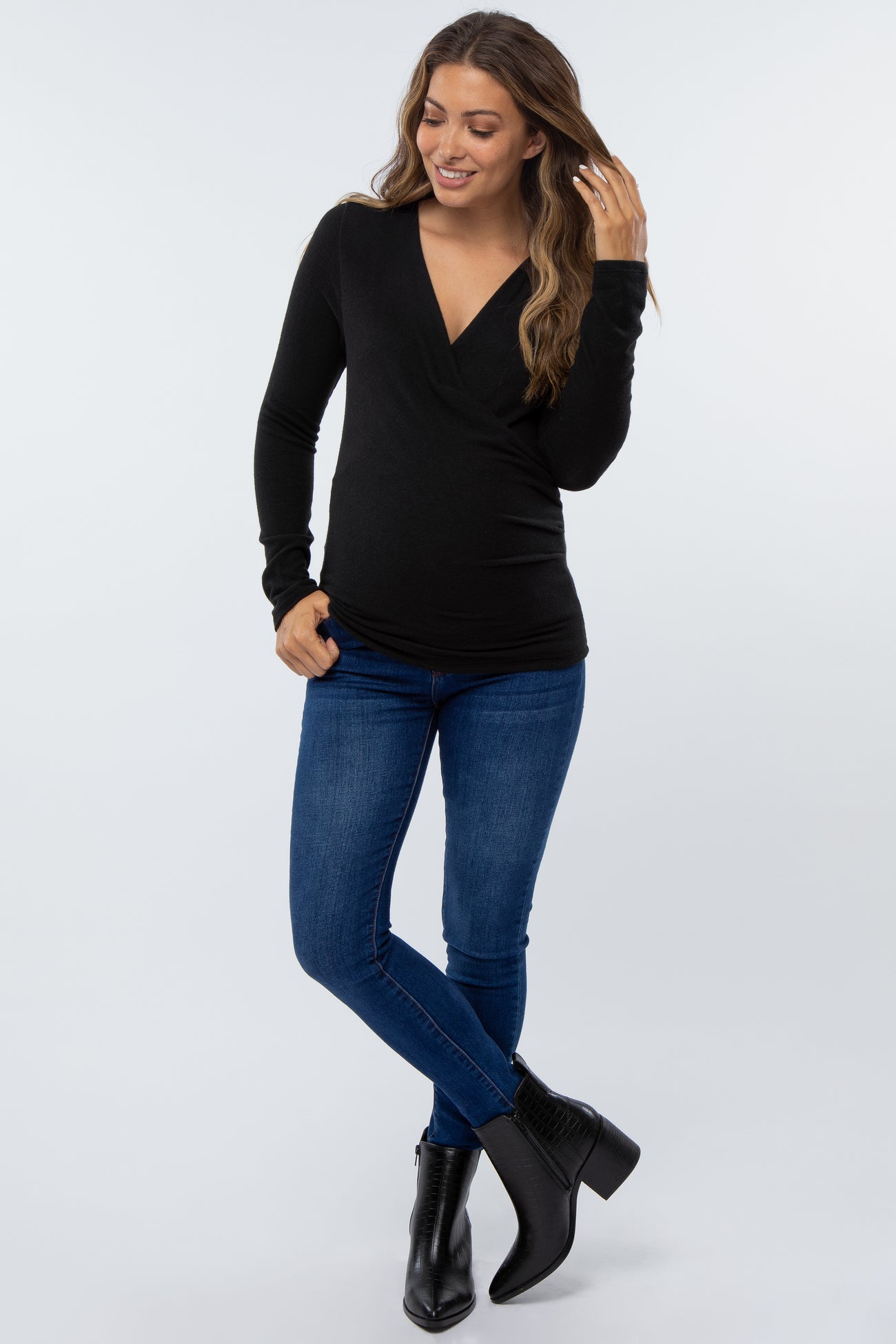 woman wearing a black long sleeve wrap top and blue skinny jeans with black ankle boots