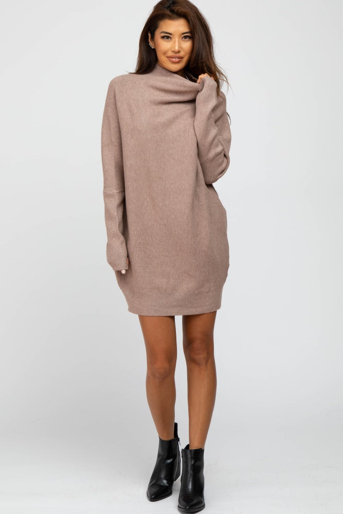woman wearing a taupe oversized sweater dress with a cowl neck and long sleeves, paired with black ankle boots