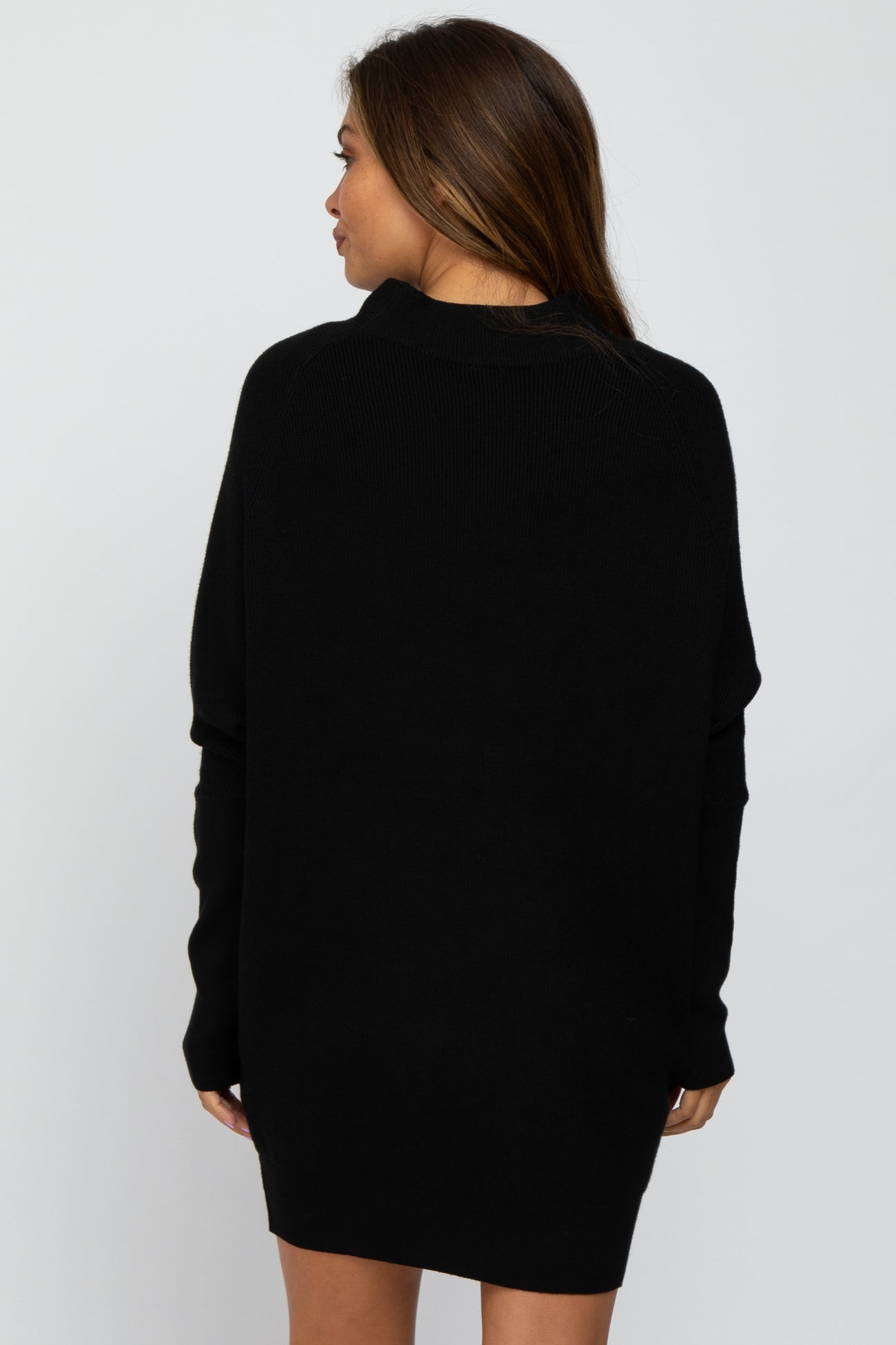 Back view of a woman wearing a black oversized mock neck sweater dress against a white background