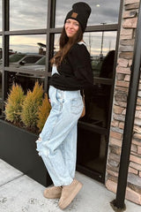 woman wearing a black long sleeve top and distressed light blue maternity overalls, showing her baby bump, standing outside
