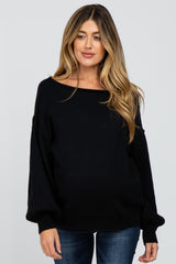 woman wearing a black off-the-shoulder maternity sweater with long sleeves and a relaxed fit, showcasing her baby bump