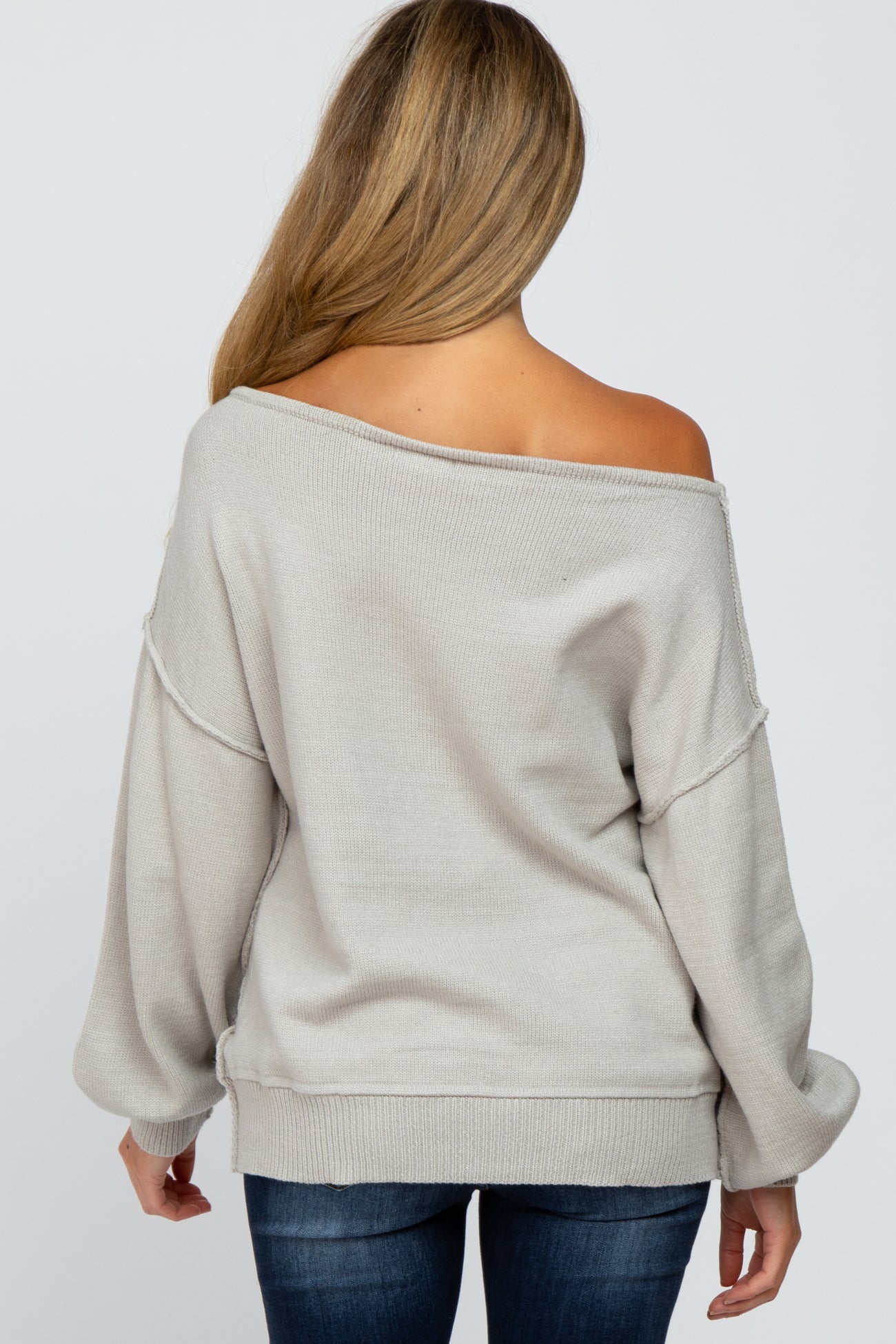 Back view of a woman wearing a light grey off-the-shoulder knit sweater and blue jeans