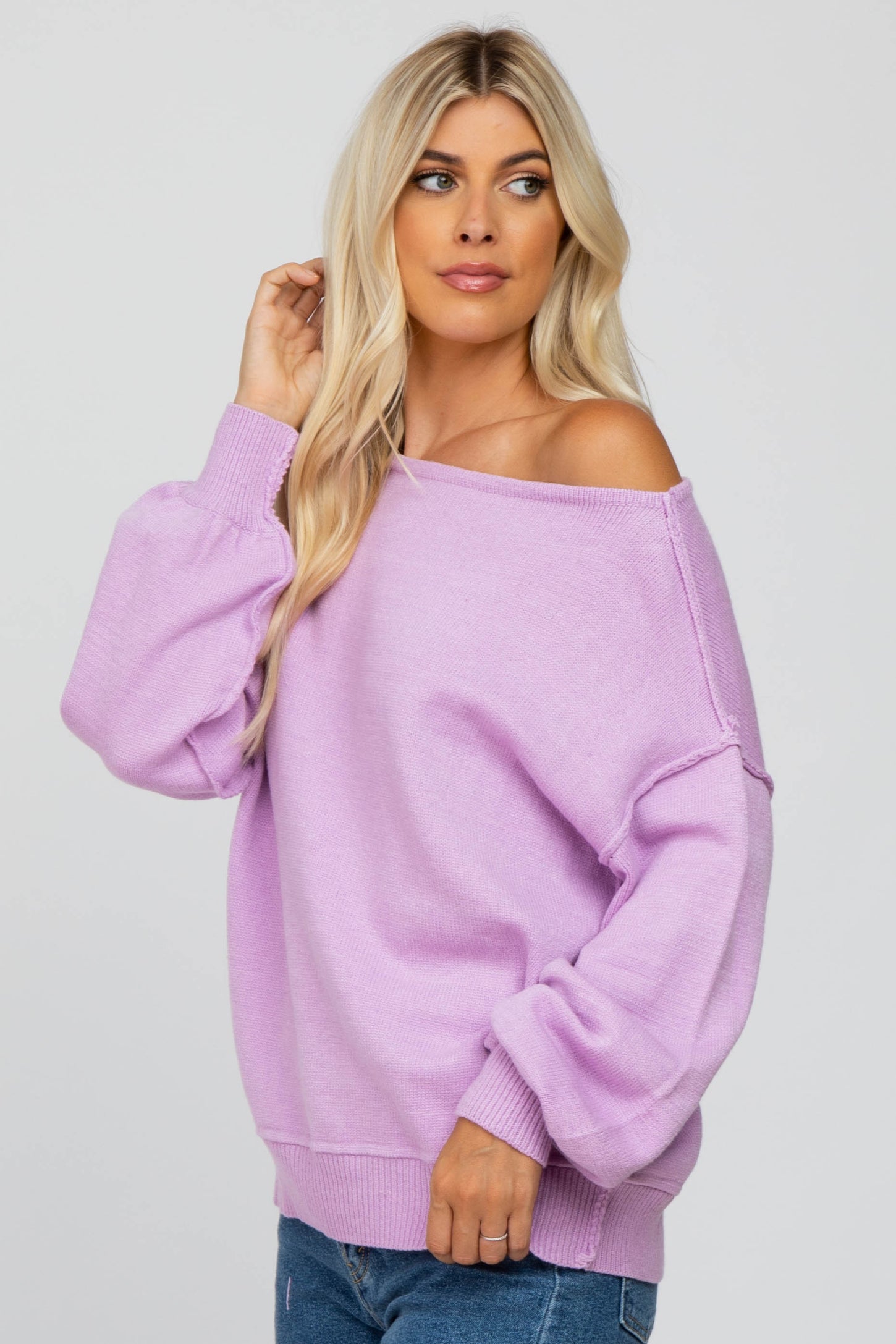 woman with blonde hair wearing a light purple off-the-shoulder knit sweater and blue jeans