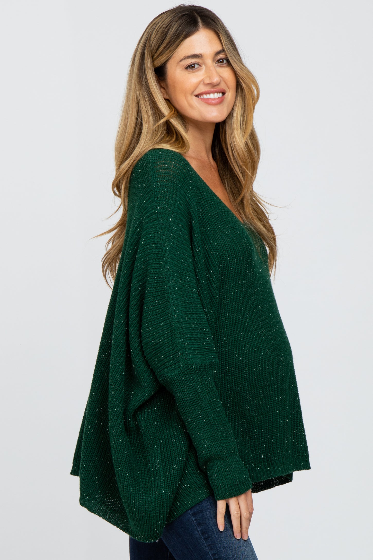 woman wearing a green maternity sweater with a deep v-neck and loose fit, showing her baby bump
