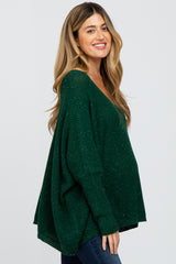 woman wearing a green maternity sweater with a deep v-neck and loose fit, showing her baby bump