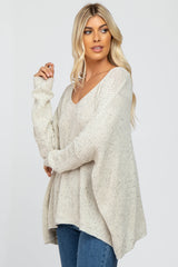 woman wearing a loose-fitting cream v-neck sweater with long sleeves and a relaxed silhouette, paired with blue jeans