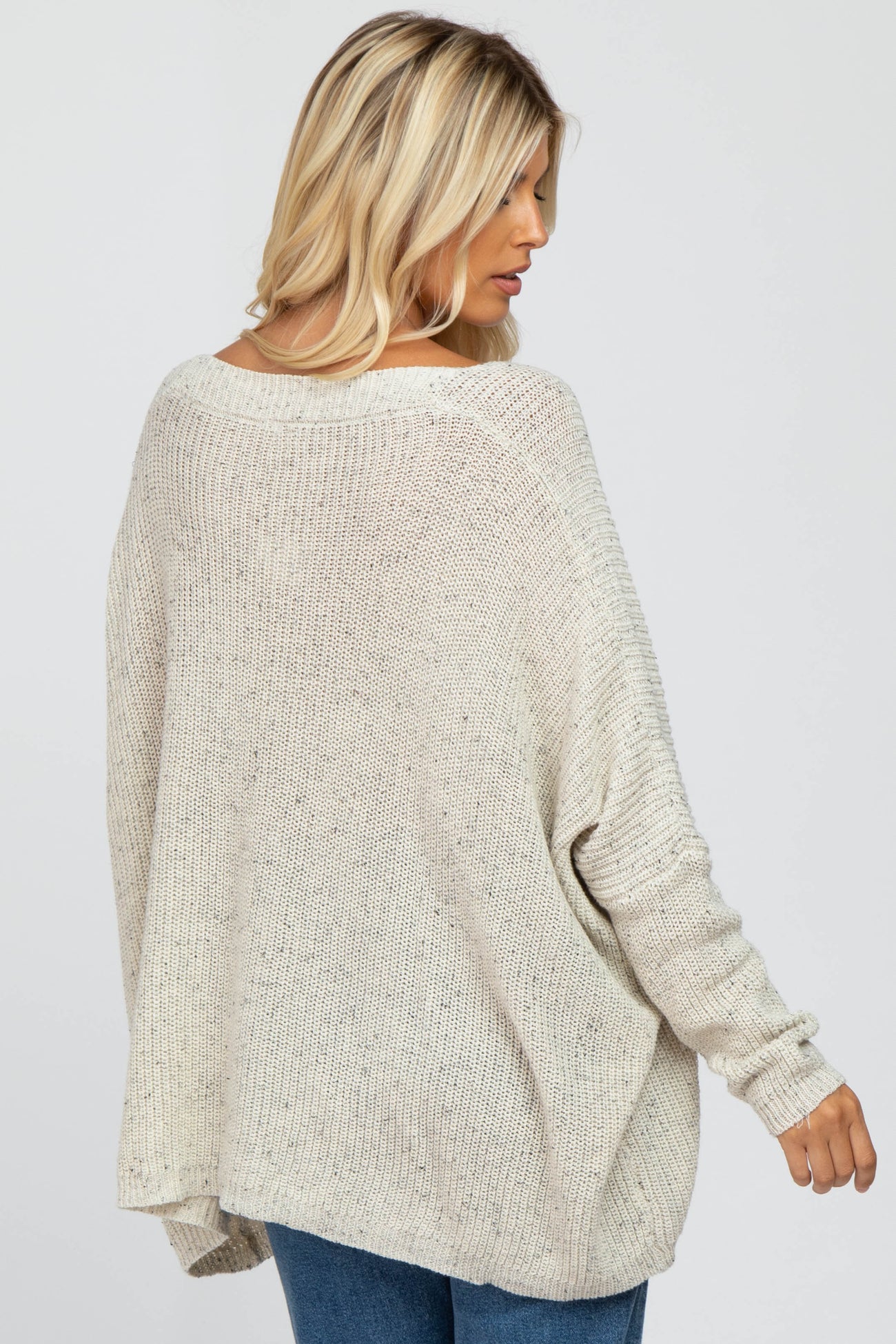 woman wearing a light beige oversized knit sweater with ribbed details, shown from the back